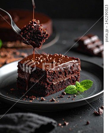 Decadent slice of dark chocolate fudge cake on a plate with a fork Decadent slice of dark chocolate fudge cake on a plate with a fork 142290823
