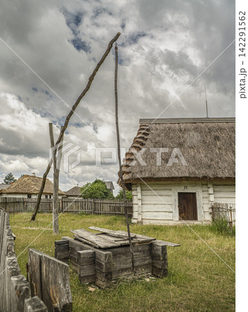 Traditional Thatched Cottage And Old Wooden Well In Rural Village Under Stormy Sky Traditional Thatched Cottage And Old Wooden Well In Rural Village Under Stormy Sky 142291562