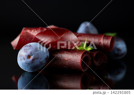 Natural plum pastila rolls with fresh plums on black background Natural plum pastila rolls with fresh plums on black background 142291805