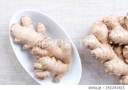 Fresh ginger root, in oval white bowl on linen. Rhizomes of Zingiber officinale, used in cooking for its flavor, and in traditional folk medicine to relieve nausea, and reduce inflammation. Photo Fresh ginger root, in oval white bowl on linen. Rhizomes of Zingiber officinale, used in cooking for its flavor, and in traditional folk medicine to relieve nausea, and reduce inflammation. Photo 142291921