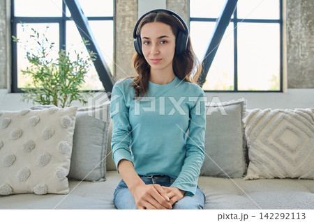 Young woman in headphones looking at camera on video call at home 142292113