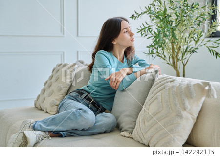 Pensive teen student girl sitting thoughtful on sofa leaning hand Pensive teen student girl sitting thoughtful on sofa leaning hand 142292115