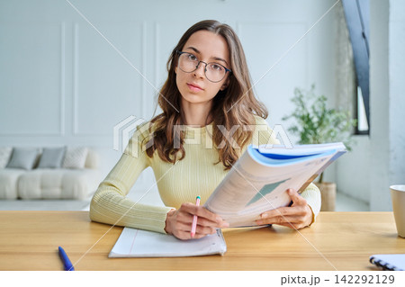 Young female student sitting at desk holding textbook webcam view 142292129