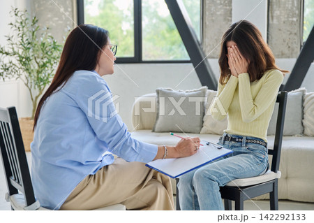 Upset young woman covering face during therapy session with psychologist Upset young woman covering face during therapy session with psychologist 142292133