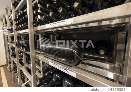 Wine bottles resting on metal shelves in wine cellar aging Wine bottles resting on metal shelves in wine cellar aging 142293234