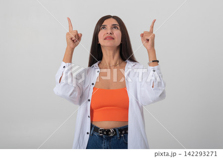 Young woman looking up with arms raised and index fingers pointing to blank space above, suggesting attention, direction or presentation space for message or advertisement Young woman looking up with arms raised and index fingers pointing to blank space above, suggesting attention, direction or presentation space for message or advertisement 142293271