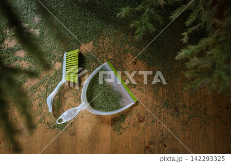 Sweeping fallen Christmas tree needles with brush and dustpan Sweeping fallen Christmas tree needles with brush and dustpan 142293325