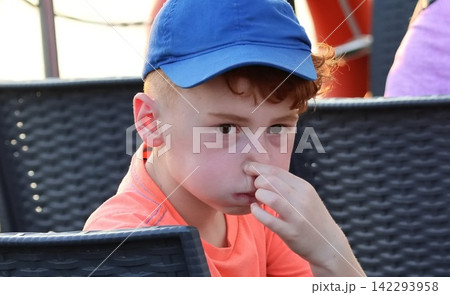 close-up shot of a little boy covering his nose because something smells bad there. 142293958