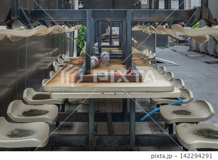 A symmetry-driven perspective of stacked outdoor dining tables and weathered plastic chairs, capturing a quiet moments of closure or seasonal transition. 142294291