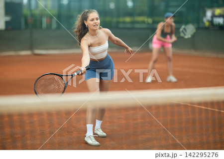 Sporty young girl playing doubles tennis on outdoor court Sporty young girl playing doubles tennis on outdoor court 142295276