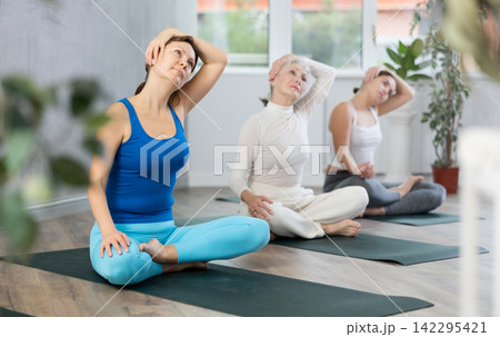 Group of sporty woman practicing yoga pose Gomukhasana in yoga studio 142295421
