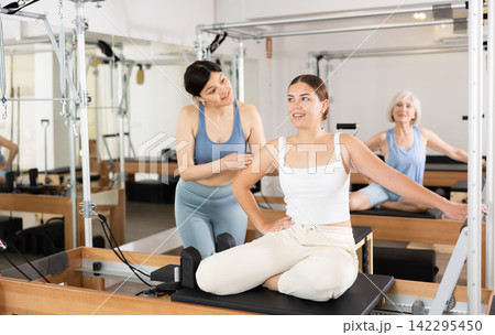 Woman doing pilates in fitness studio with female personal trainer controlling movements Woman doing pilates in fitness studio with female personal trainer controlling movements 142295450