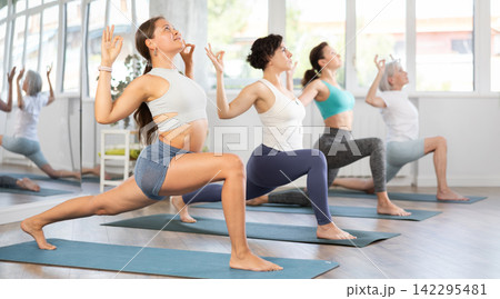 Woman performing revolved side angle pose Parivrtta Parsvakonasana during yoga class with female group in fitness studio 142295481