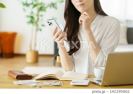 スマホを操作ながら困った顔をするミドルエイジの日本人女性の手元のアップ 142295602