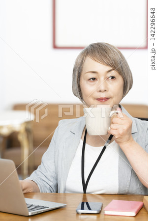 オフィスで仕事をしながらコーヒーを飲むシニア女性 142296648