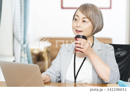 オフィスで仕事をしながらコーヒーを飲むシニア女性 142296651