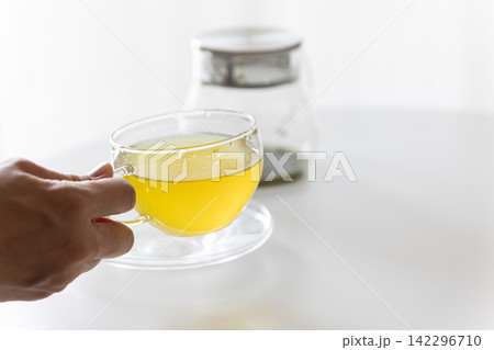 白テーブルの上に置かれた透明なガラス急須とグラスに入った温かい緑茶・日本茶 142296710