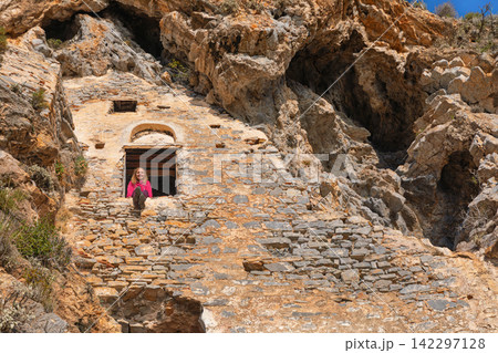 Woman looking at beautiful view from window of Afkule monastery carved into high vertical cliffs near Oludeniz, Turkey. Dramatic rock landscape and historic architecture. Travel, cultural destination. Woman looking at beautiful view from window of Afkule monastery carved into high vertical cliffs near Oludeniz, Turkey. Dramatic rock landscape and historic architecture. Travel, cultural destination. 142297128