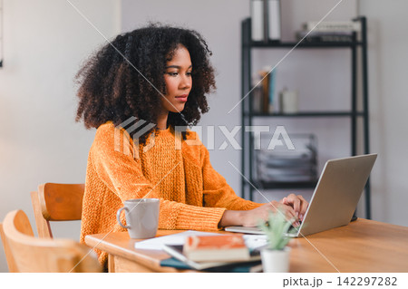 Smiling African American woman using a laptop while working from home. Smiling African American woman using a laptop while working from home. 142297282