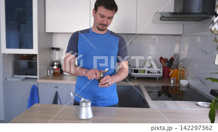 A handsome guy opens a can of fragrant coffee to brew it in a tin turk. Student's morning. Morning routines 142297362