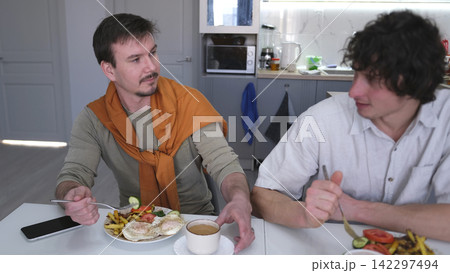 Two handsome young men are talking over a hearty lunch in a stylish kitchen. Gay men are discussing their wedding. Friends chat 142297494