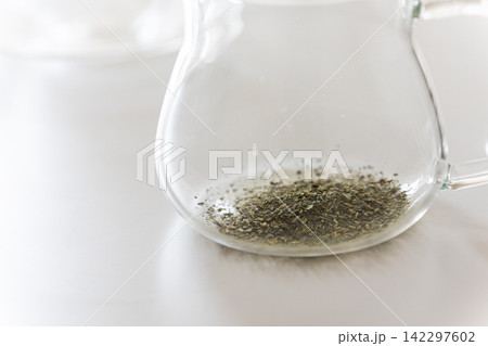 白テーブルの上に置かれた透明なガラス急須に入っている緑茶の茶葉・日本茶 142297602