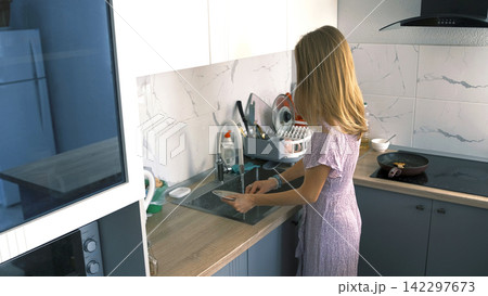 The household cares of a loving housewife. A woman washes dirty dishes after lunch in the kitchen The household cares of a loving housewife. A woman washes dirty dishes after lunch in the kitchen 142297673