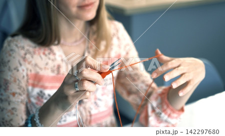 Hobbies, creativity, and art. Close-up of a woman's hands holding knitting needles and knitting with yarn. A woman knits a scarf Hobbies, creativity, and art. Close-up of a woman's hands holding knitting needles and knitting with yarn. A woman knits a scarf 142297680