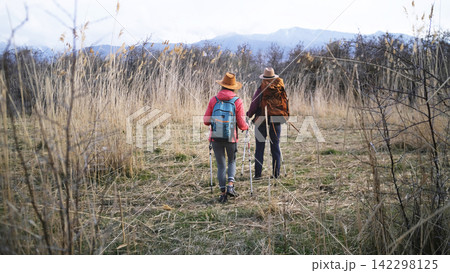 A team of two women heads into the mountains through a thicket of dry bushes, view from the back. Tourists travel together A team of two women heads into the mountains through a thicket of dry bushes, view from the back. Tourists travel together 142298125