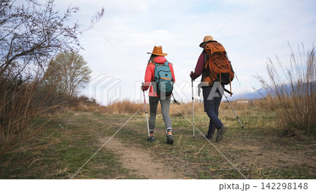 Two sisters hikers are walking towards the mountains. Weekend camping trip. Outdoor fitness. Hobbies of two students 142298148