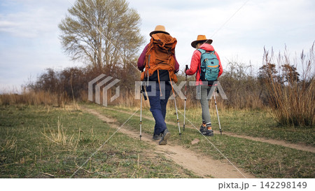 Two travelers with backpacks and trekking poles are traveling to the holy places of the planet. Two lesbians are hiking. Two tourists 142298149
