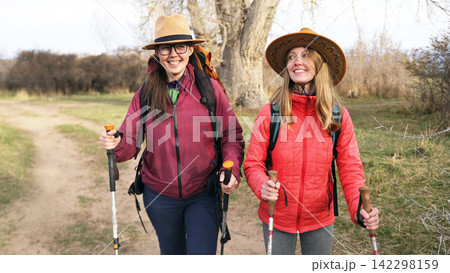 Two pretty young women are walking along the path and smiling. Close friends have fun camping. Lesbian couple walks in the park at sunset Two pretty young women are walking along the path and smiling. Close friends have fun camping. Lesbian couple walks in the park at sunset 142298159