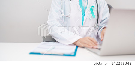 doctor using laptop and report notes on notebook. Teal and white ribbon concept of January Cervical Cancer Awareness month, September Ovarian Cancer, PCOS, April Sexual Assault 142298342