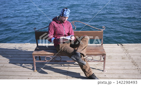 When the Internet was turned off. A handsome young man is sitting on a bench by the water and reading a book. The scene is romantic 142298493