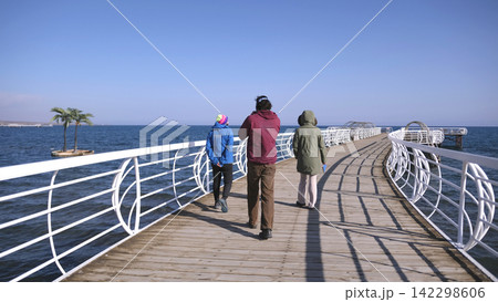 Issyk Kul Lake boardwalk in Kyrgyzstan. Three friends are walking along the pier on a sunny day. The scene is peaceful and relaxing 142298606