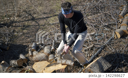 A farmer in a blue bandana is chopping firewood on a garden plot on a sunny, clear day. The man is wearing a black shirt and khaki trousers A farmer in a blue bandana is chopping firewood on a garden plot on a sunny, clear day. The man is wearing a black shirt and khaki trousers 142298627