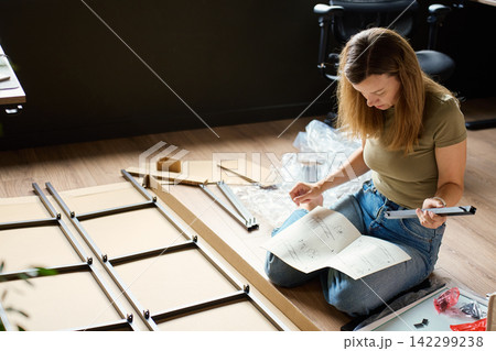 Woman reading instructions while assembling shelf at home Woman reading instructions while assembling shelf at home 142299238