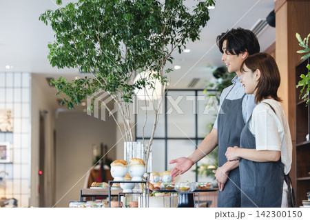 カフェのカウンターで料理を案内する男女スタッフ カフェのカウンターで料理を案内する男女スタッフ 142300150