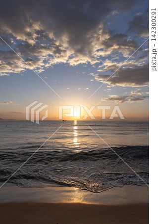 A peaceful golden sunset casts warm light across a calm ocean and sandy beach A peaceful golden sunset casts warm light across a calm ocean and sandy beach 142300291