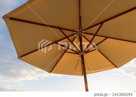 Sunlit beach umbrella photographed from below, showing wooden ribs and canvas canopy Sunlit beach umbrella photographed from below, showing wooden ribs and canvas canopy 142300293