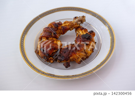 Close-up view of roasted tandoori chicken leg pieces served on white ceramic plate. Delicious grilled chicken legs with spices ready to eat for meal. 142300456