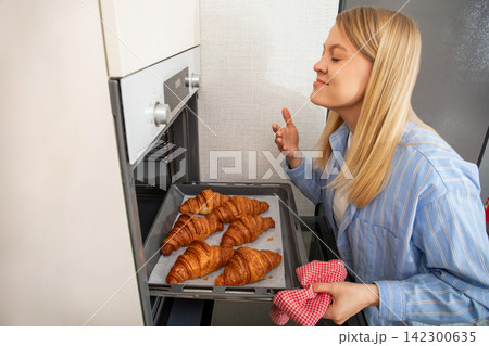 Baking. Woman enjoys aroma of golden croissants just taken from oven. Baking concept Baking. Woman enjoys aroma of golden croissants just taken from oven. Baking concept 142300635