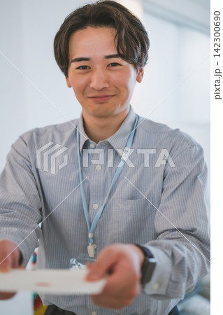笑顔で封筒を差し出す20代ビジネスマンのオフィスラブシーン 142300690