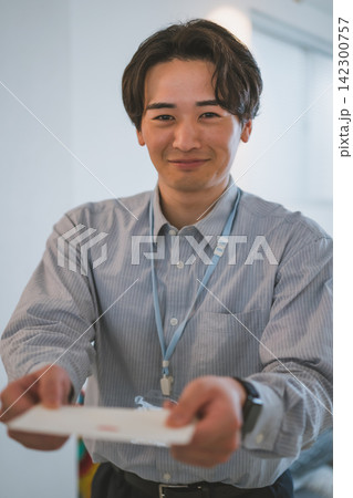 笑顔が輝く封筒を差し出す20代ビジネスマンのオフィスラブシーン 笑顔が輝く封筒を差し出す20代ビジネスマンのオフィスラブシーン 142300757