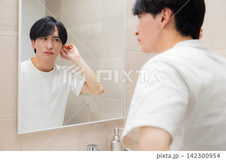 洗面所で鏡を見る若い男性 洗面所で鏡を見る若い男性 142300954