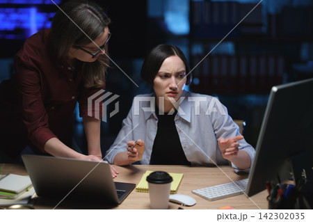 Businesswomen review computer problem during night shift Businesswomen review computer problem during night shift 142302035