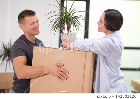 Joyful married couple with box and plant smiles in apartment Joyful married couple with box and plant smiles in apartment 142302126