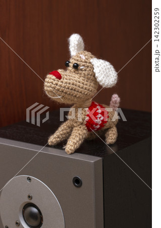 A knitted wool dog stands on a speaker. 142302259