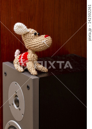 A knitted wool dog stands on a speaker. 142302261