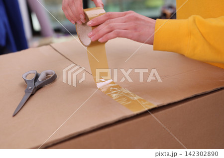 Woman hands pack cardboard box with adhesive tape at home 142302890